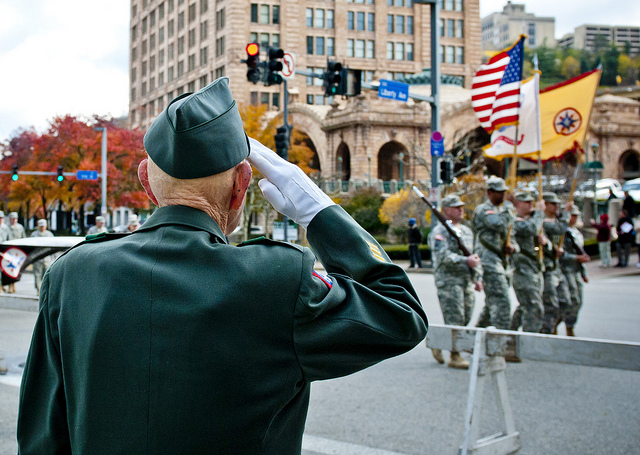 World War II veteran in dress uniform salutes the American flag as it passes in a parade