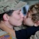 An army soldier receives a kiss from their child.