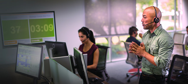 A call-center worker in a headset stands while talking with a customer about gated, exclusive offers.