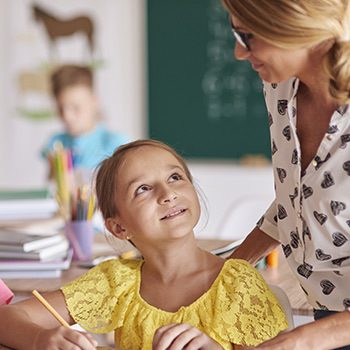 A teacher helping a young student. Marketing to teachers with exclusive offers is a great way to thank them for their service and acquire loyal customers.