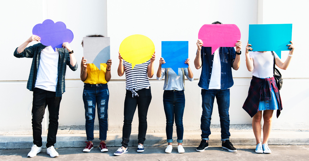 College students standing in a line covering their faces with cut outs of chat bubbles.