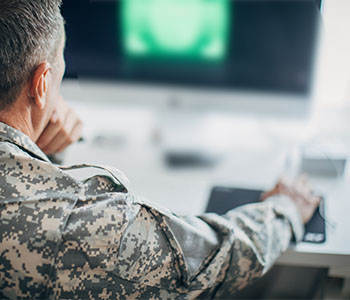 A photo looking over the shoulder of a middle-aged military officer at his computer.