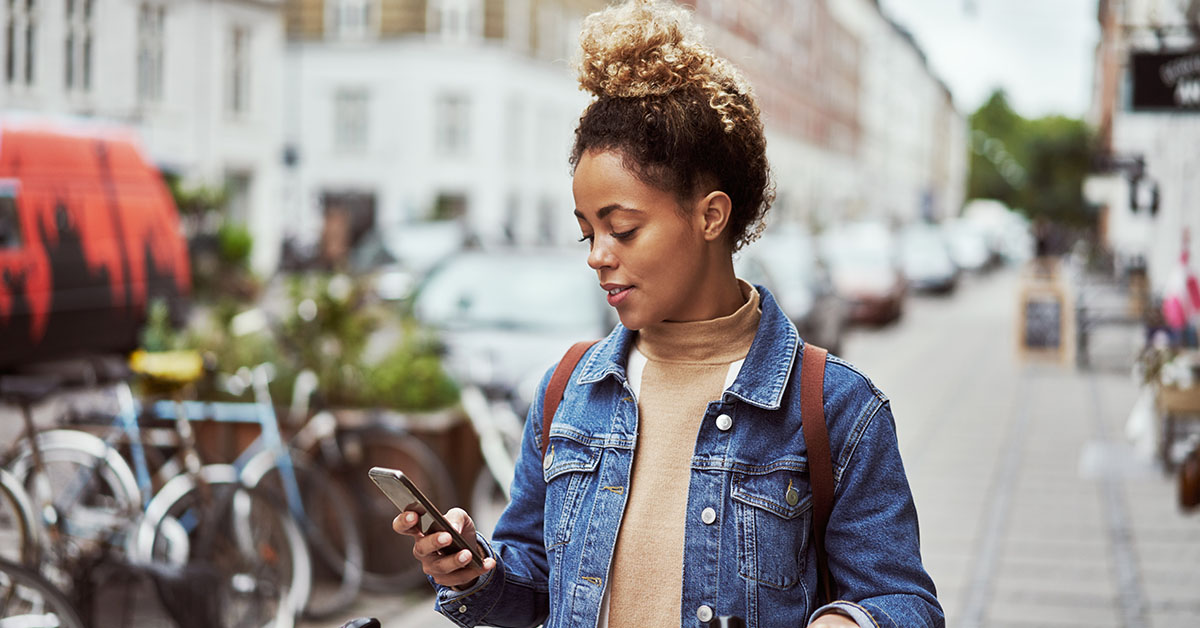 A young woman on the street using customer verification software on her mobile phone to redeem a personalized offer.