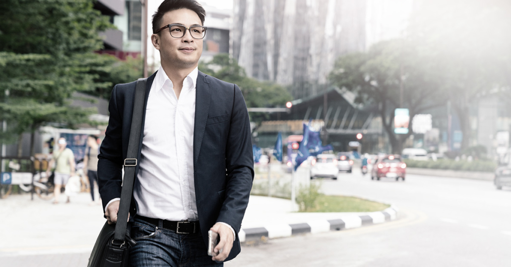 A man in a blazer walking through a plaza with a discounted messenger bag he bought using employee verification.