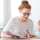 A smiling female teacher helps a young student using school supplies she bought with a personalized offer.