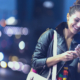 A woman on a street at night, smiling at her cell phone after receiving a personalized offer through an affiliate marketing program.