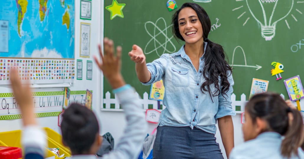 A female teacher calling on a young student in her classroom.