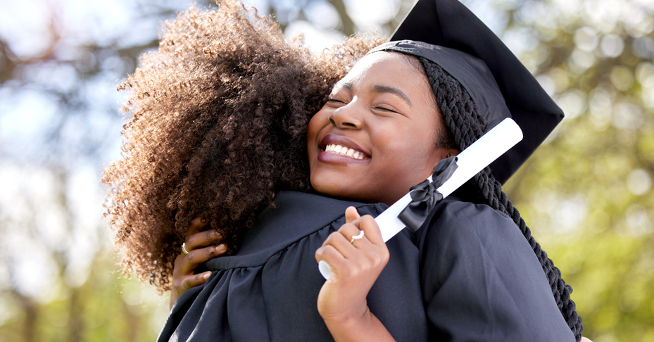 Two recent graduates hugging wearing cap and gown.