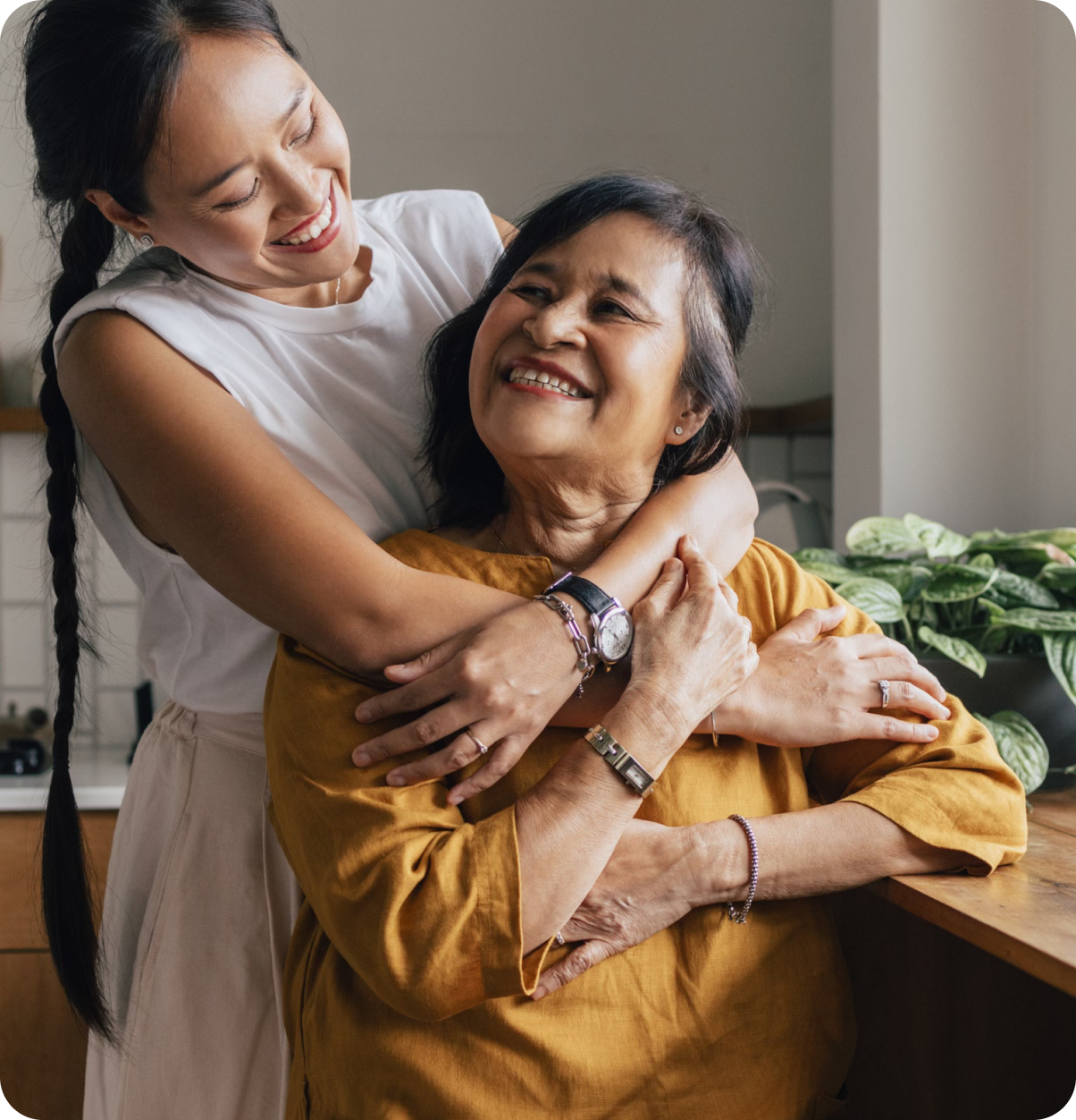Smiling younger woman embraces smiling older adult.