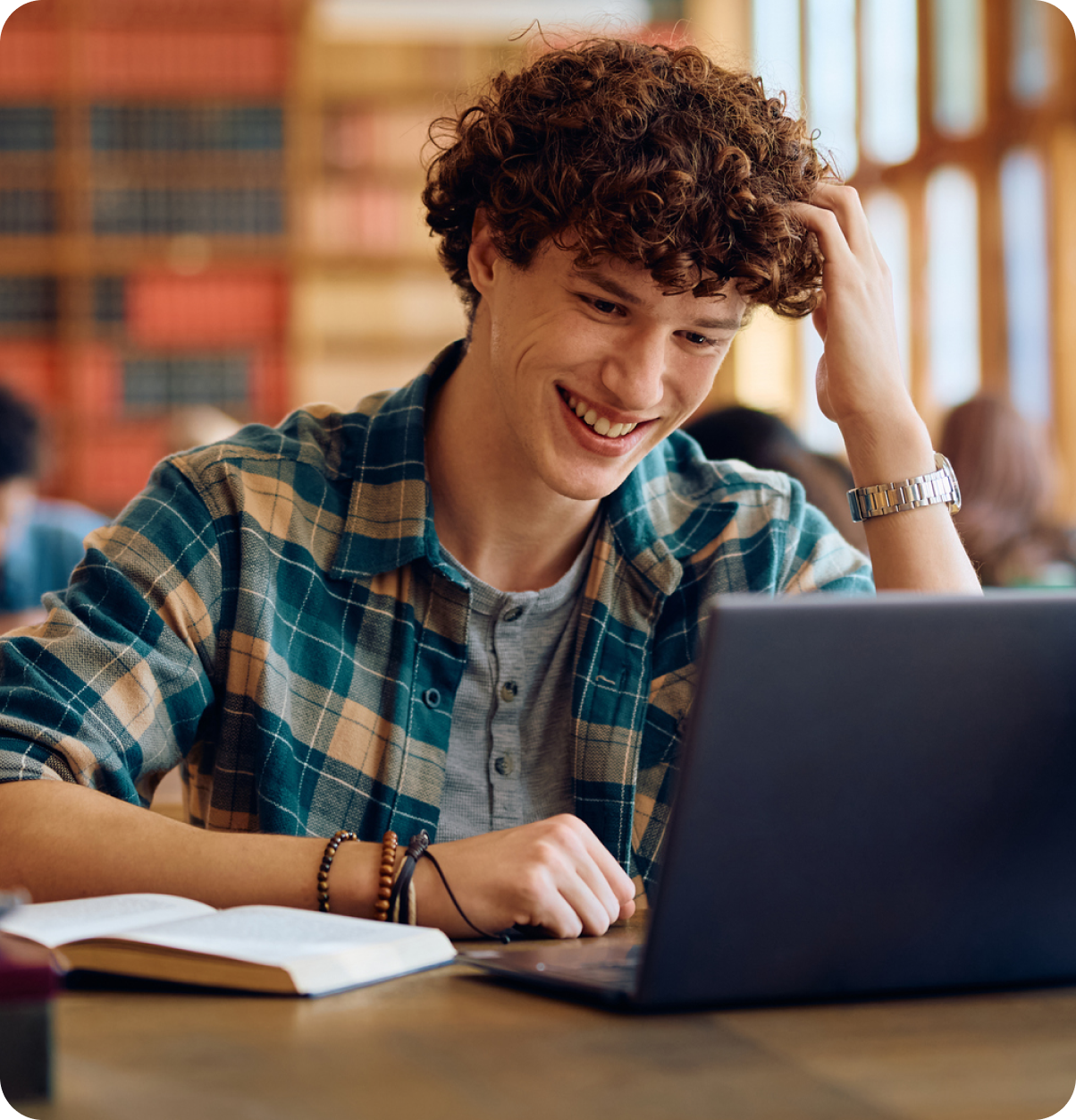 Student smiling in library using laptop.
